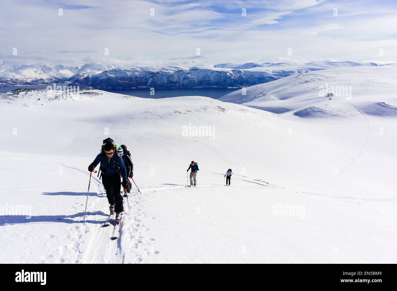 Skiers ski touring with tracks from a mountain hut on way up Rornefjellet above Lyngenfjord Lyngen Alps Troms County Norway Stock Photo