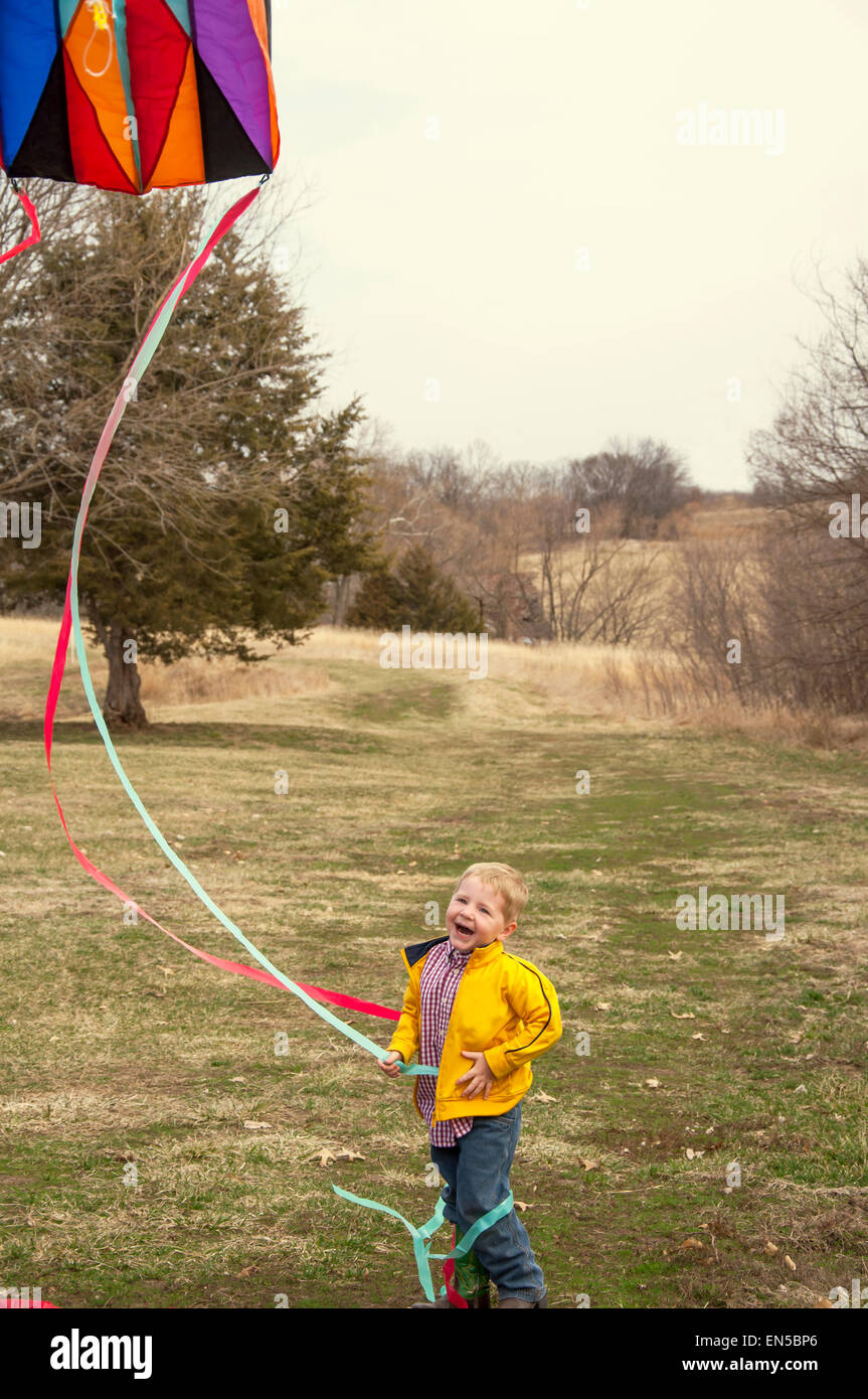 boy holding tail of flying kite laughing Stock Photo