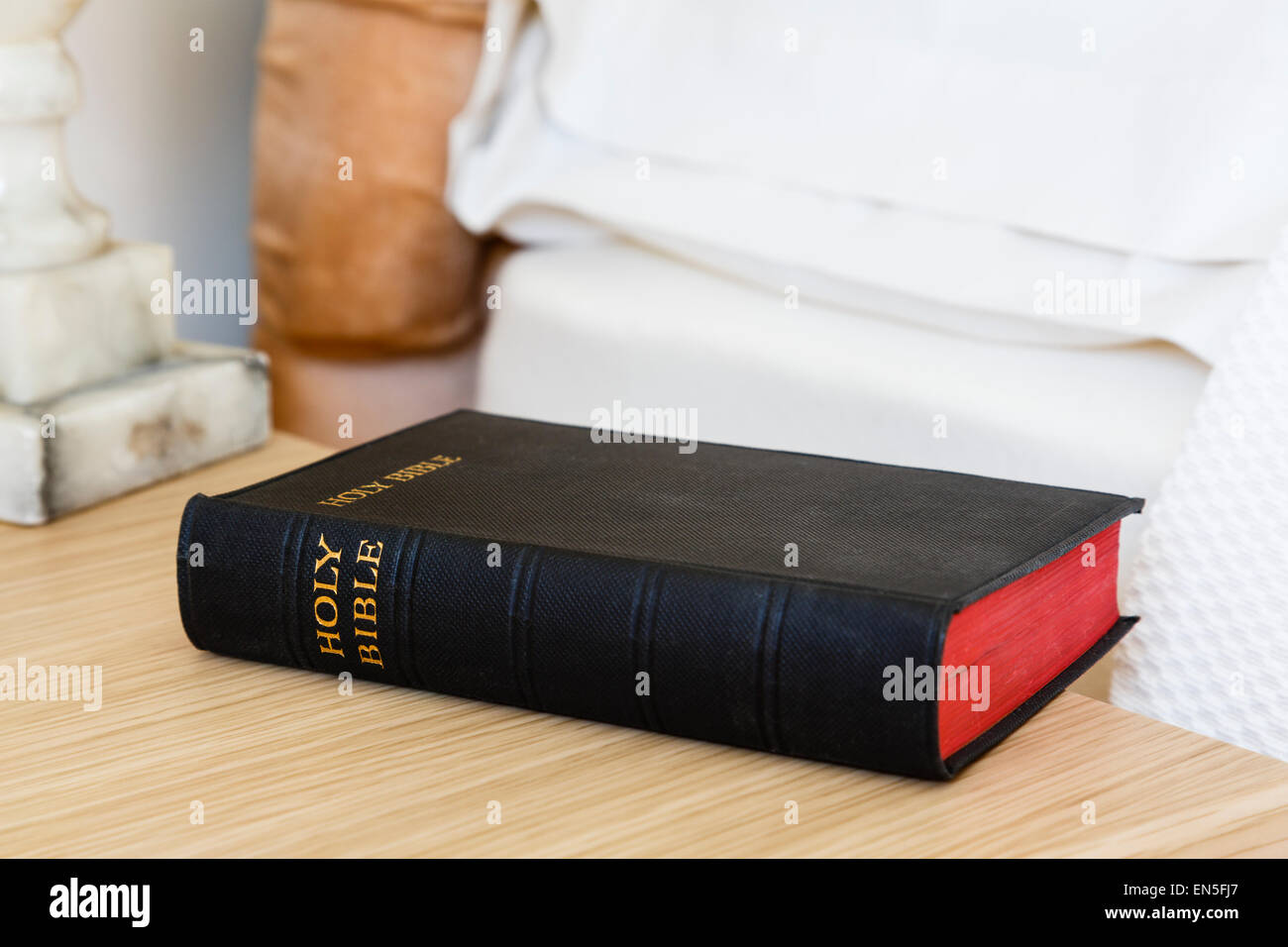 English Holy Bible book on a bedside table beside a bed in a bedroom. England, UK, Britain, Europe Stock Photo