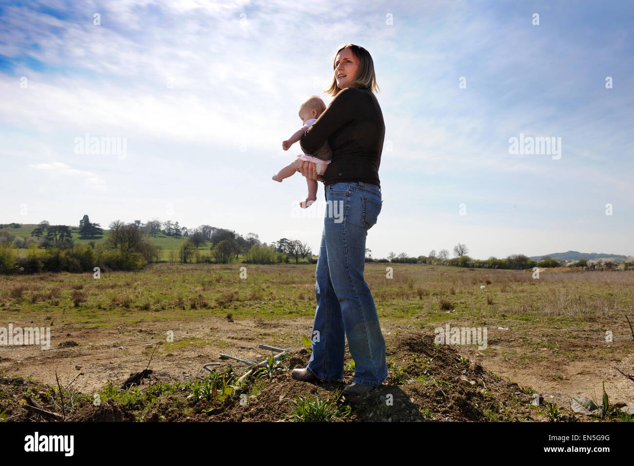Young mother and baby on a brownfield site with adjoining Newbuild housing earmarked for development UK Stock Photo