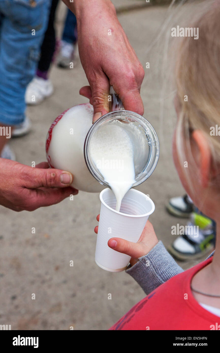 Farmer holding glass jug pouring fresh milk in little girl's plastic cup at farm Stock Photo