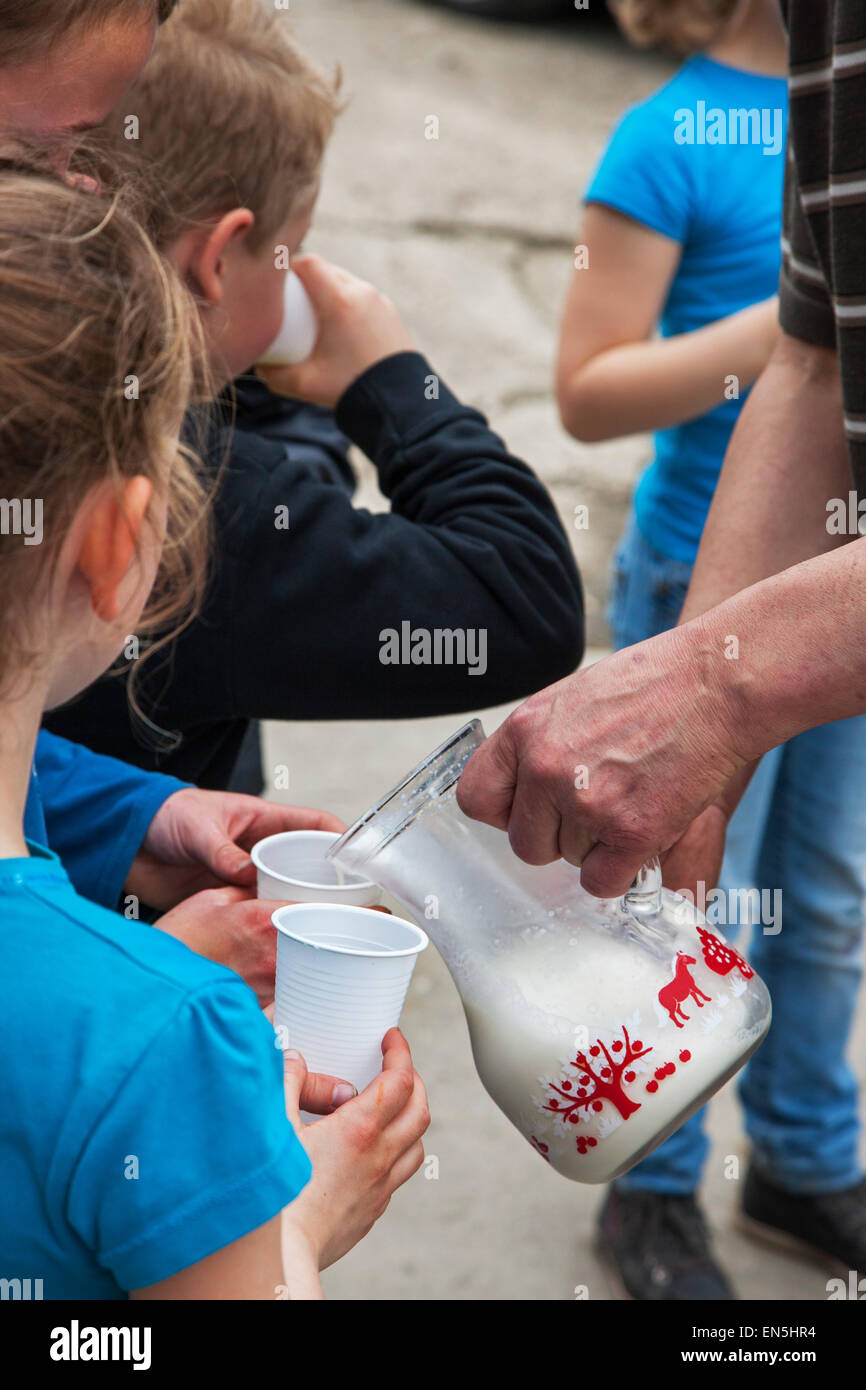 Farmer holding glass jug pouring fresh milk in little children's plastic cups at farm Stock Photo