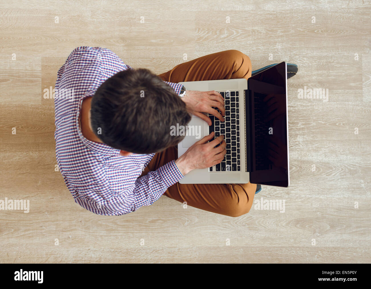 Top view of young man sitting on the floor and working with a laptop ...
