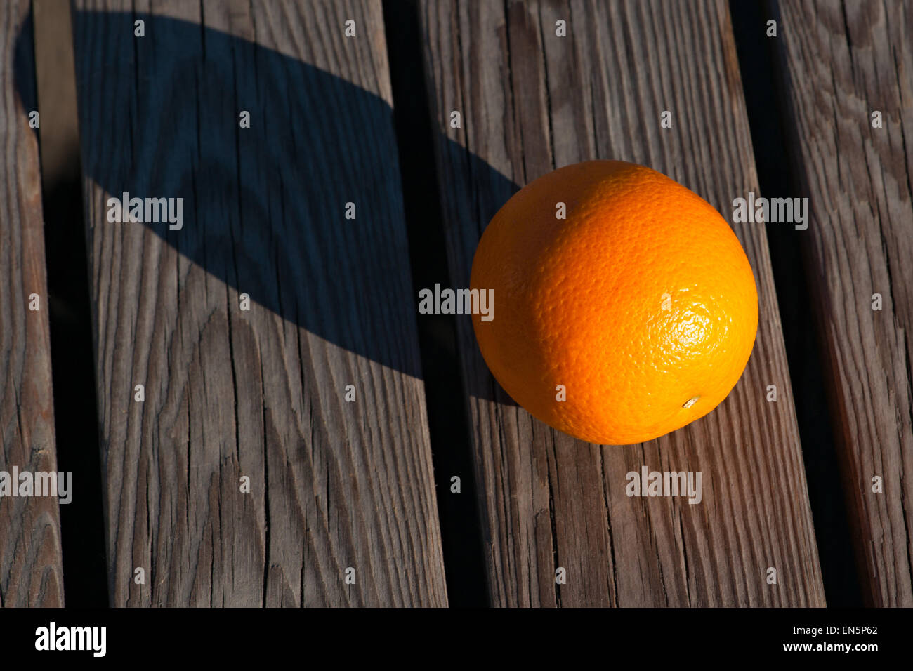 Orange fruit on a wooden bench in incline sunlight. The fruit casts the long shadow. Play of light and shadow Stock Photo