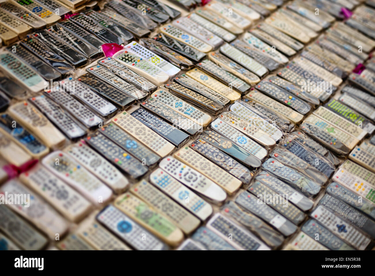 Dozens of second-hand remote control wands from a wide array of electronic devices displayed for sale at a vendor's stand in Sin Stock Photo