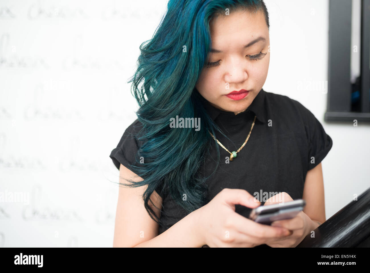 Asian woman with blue hair texting on smartphone Stock Photo
