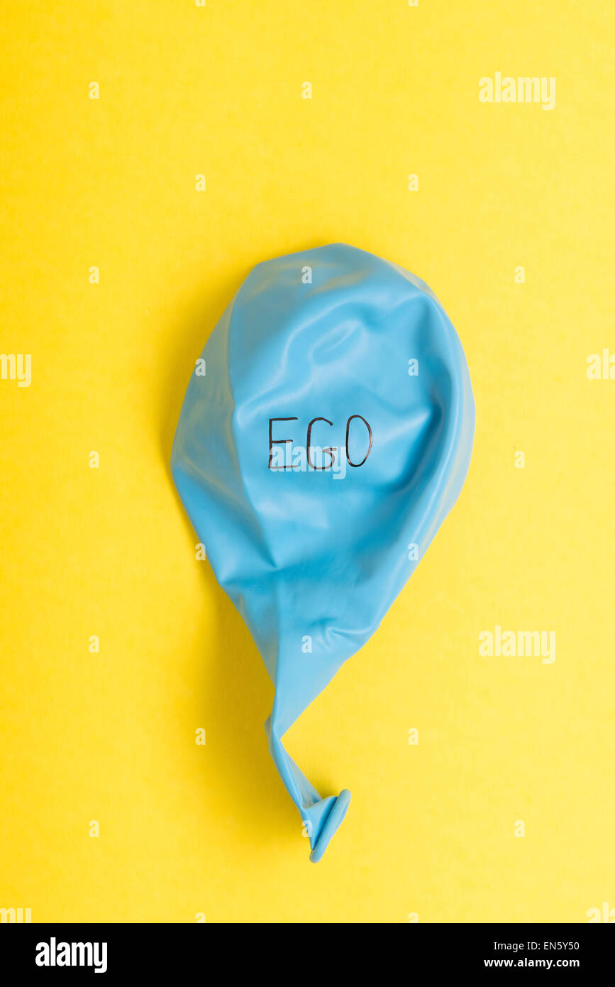 Deflated blue balloon on yellow background with the word ego on it Stock Photo