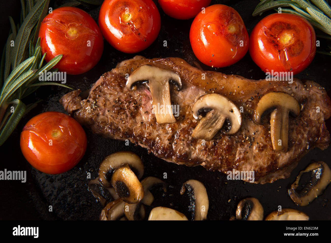 Grilling Strip Loin Steak in Cast Iron Frying Pan: Steak  is cooked  and sliced  - shown with grilled tomatoes and mushrooms Stock Photo