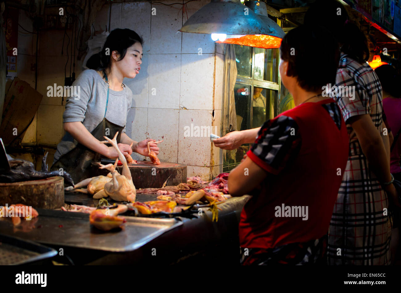 Customer buying fresh poultry from a young female butcher in an Asian market. Indoor market; Guangzhou, China; woman; women; customers Stock Photo