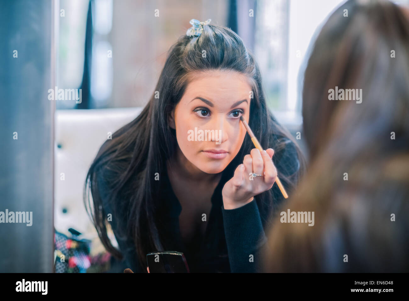 Attractive brunette woman  applying eye shadow as seen in mirror Stock Photo