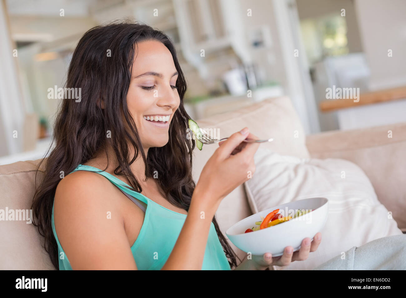 Pretty brunette eating salad on couch Stock Photo