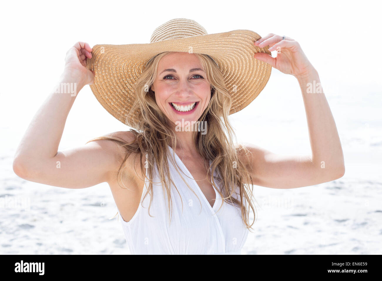 Smiling blonde in white dress looking at camera and wearing straw hat ...