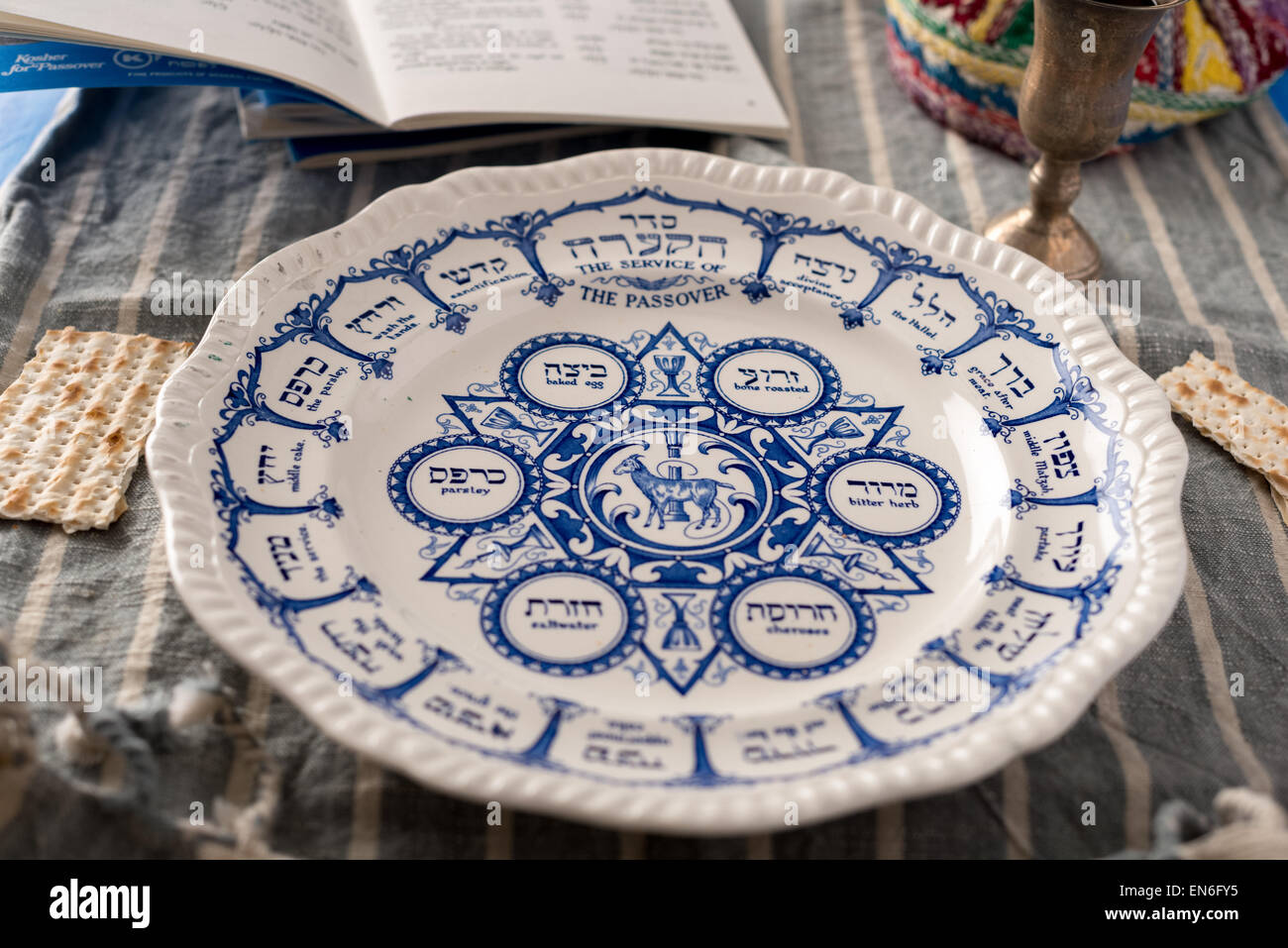 Vintage traditional passover plate, used during the Jewish holiday is show with the habbadah, kiddush cup and colourful yarmulke Stock Photo