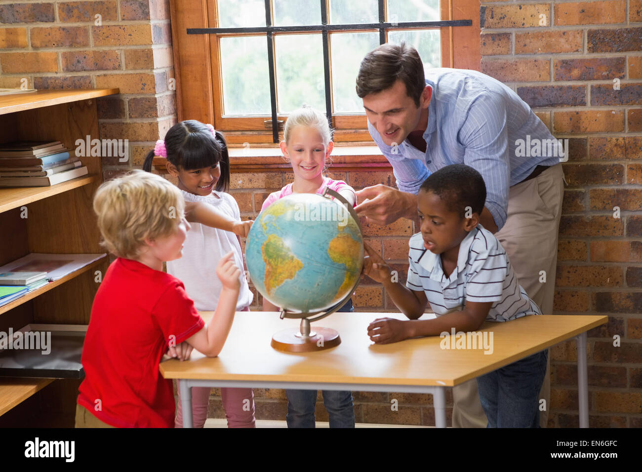 Cute pupils and teacher looking at globe in library Stock Photo - Alamy