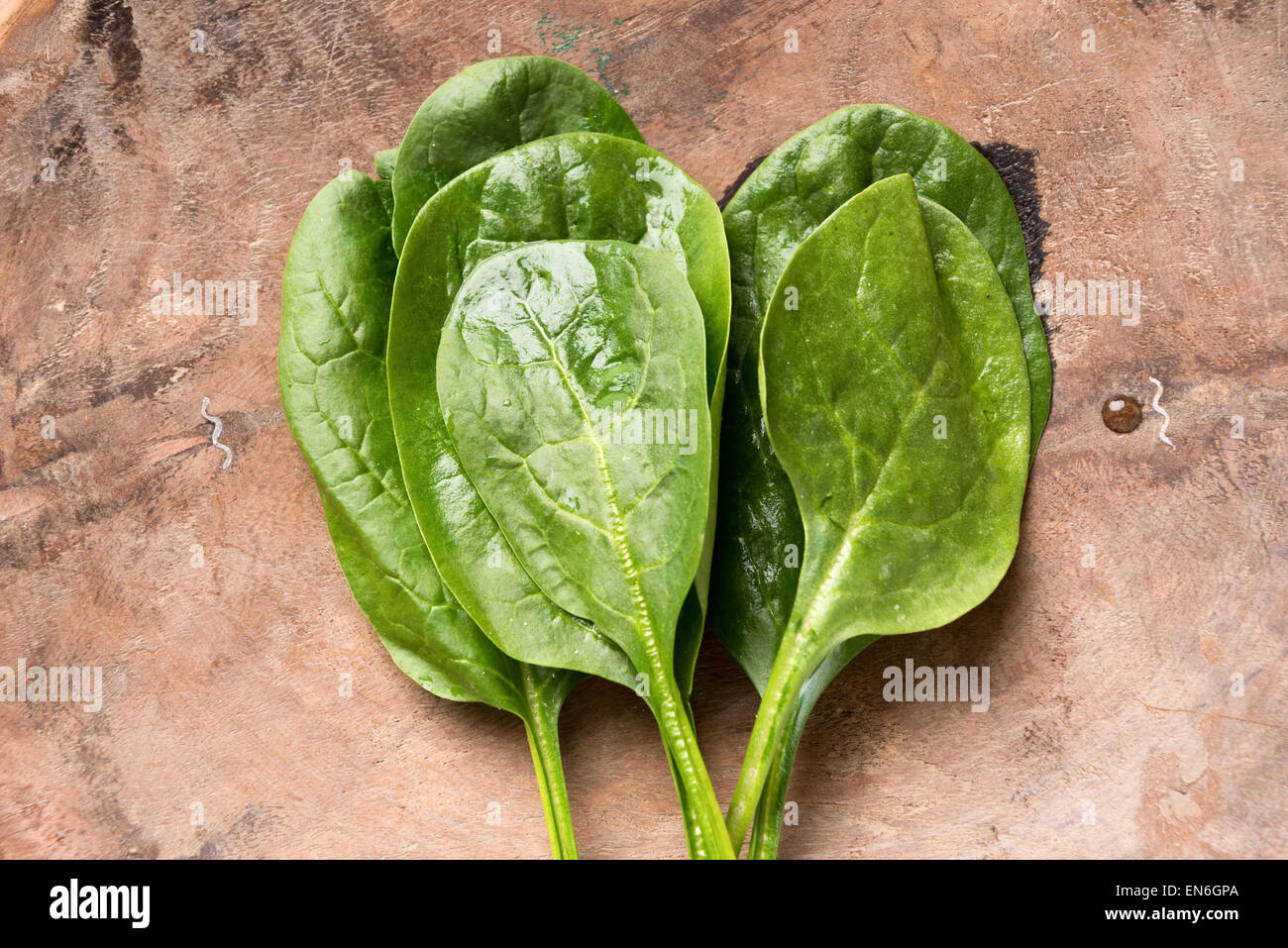 Fresh raw spinach is a rustic wooden bowl set on wood table with copy space Stock Photo