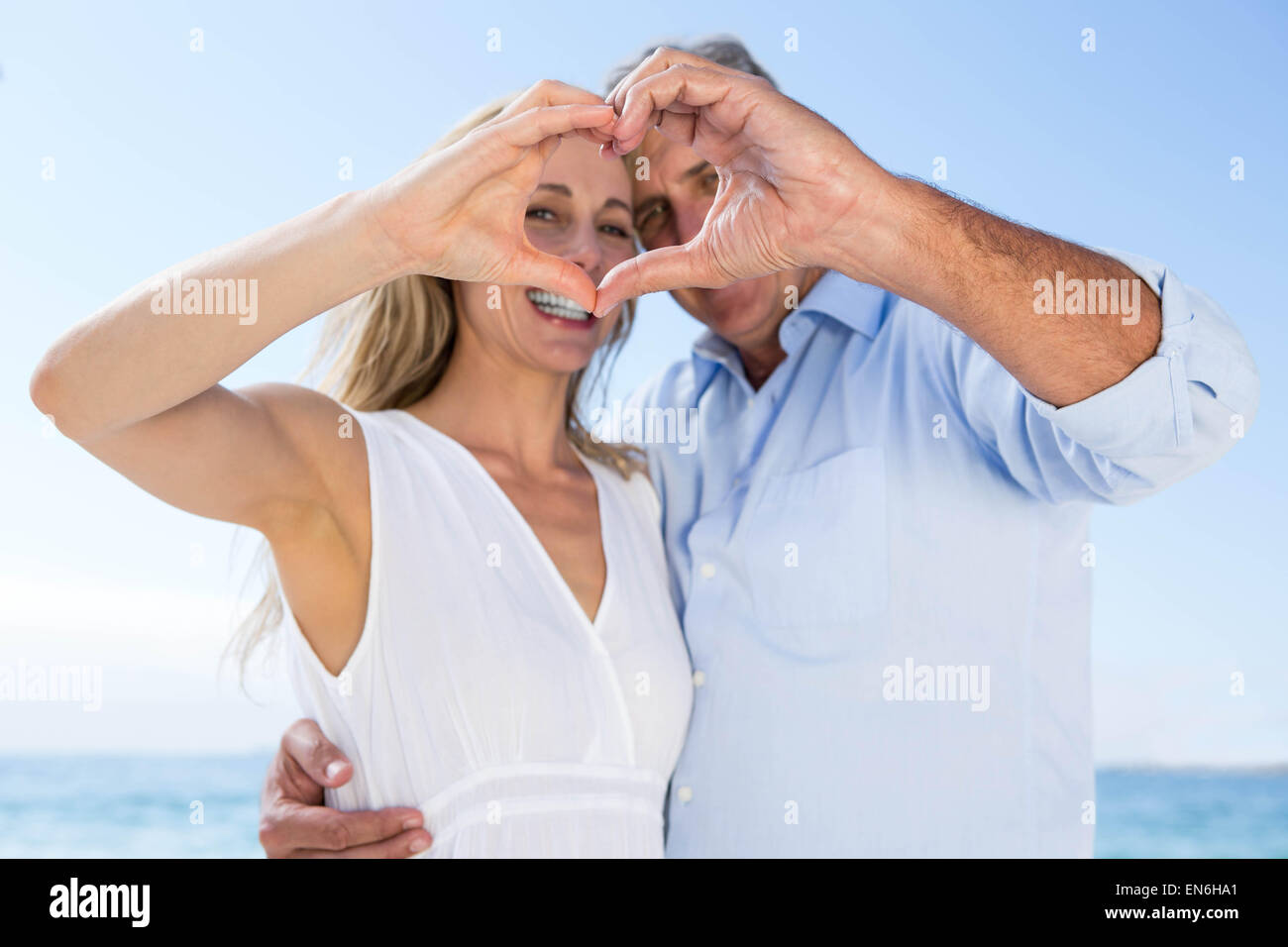 Happy couple smiling at camera and doing heart shape with their hands ...