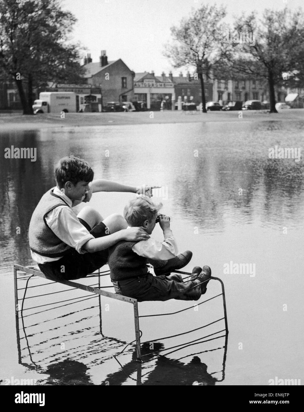 Two boys sitting on an old fire guard on the edge of a lake. 1st July 1955 Stock Photo