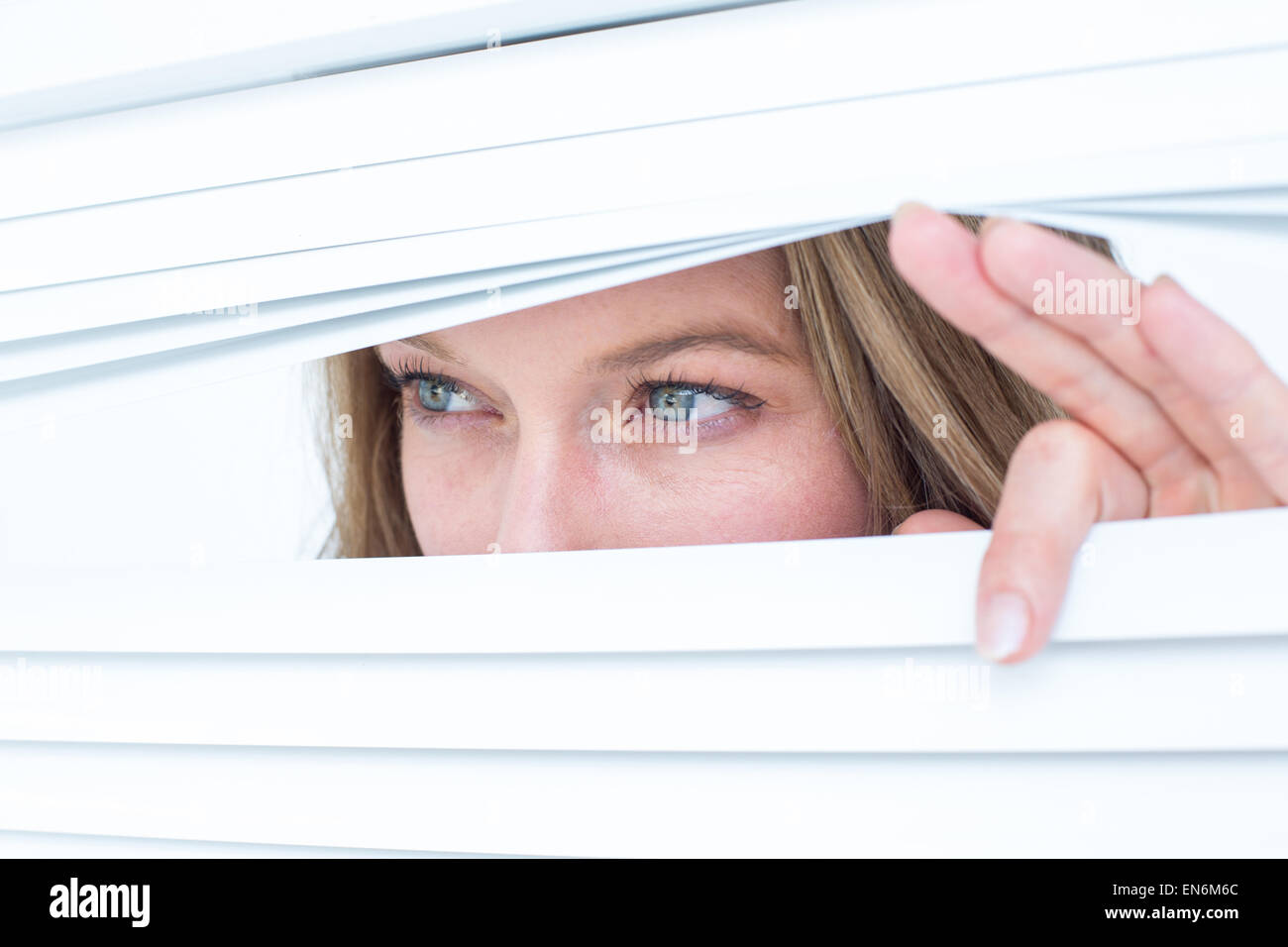 Woman peering through roller blind Stock Photo