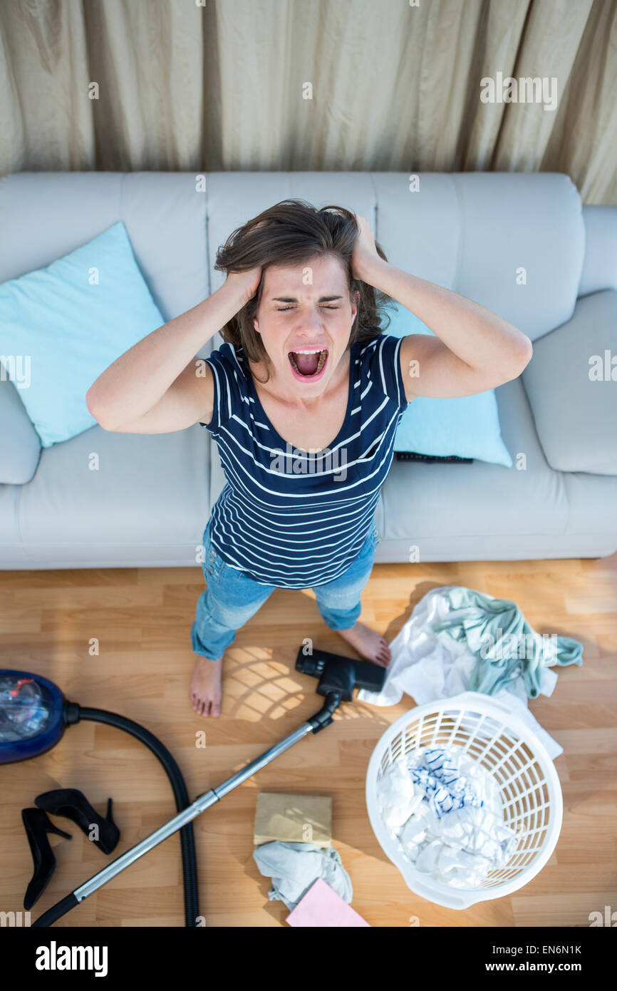 Angry woman in a chaotic living room with vacuum cleaner Stock Photo