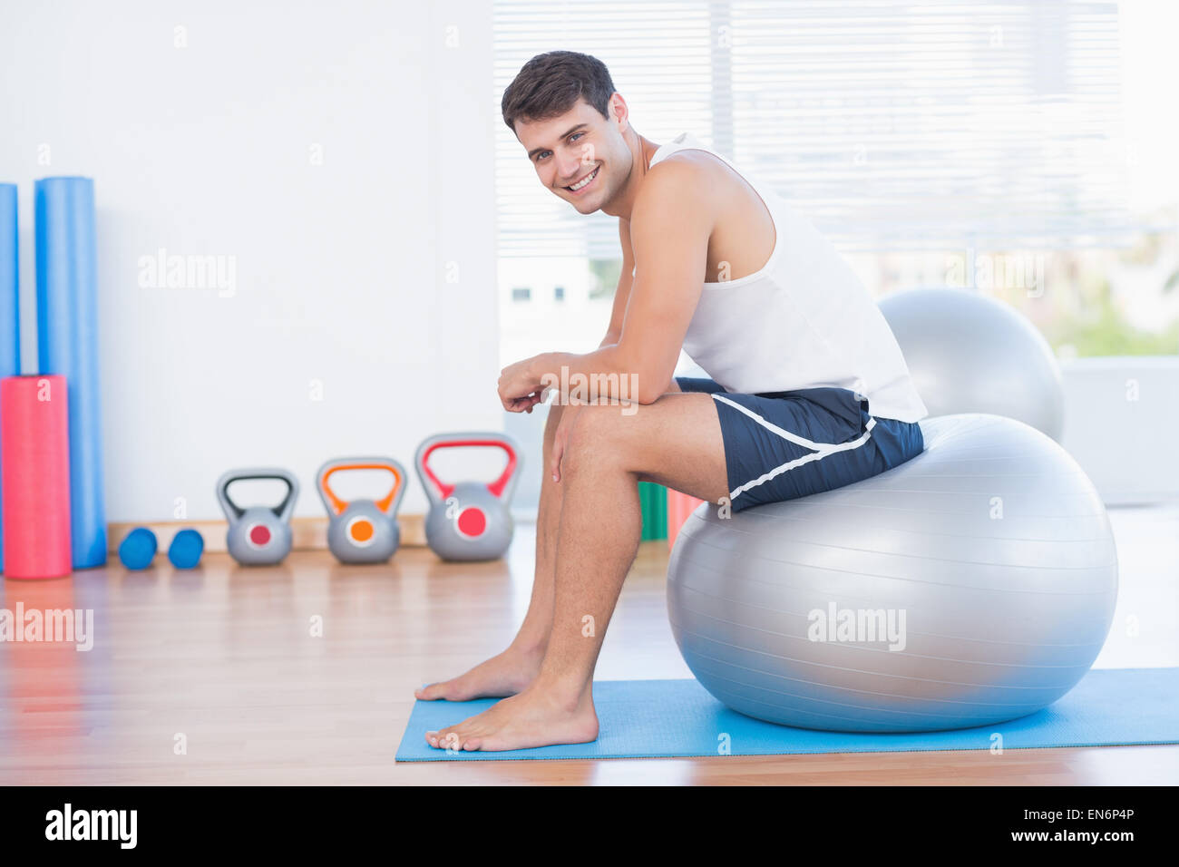 Smiling man sitting on exercise ball and looking at camera Stock Photo