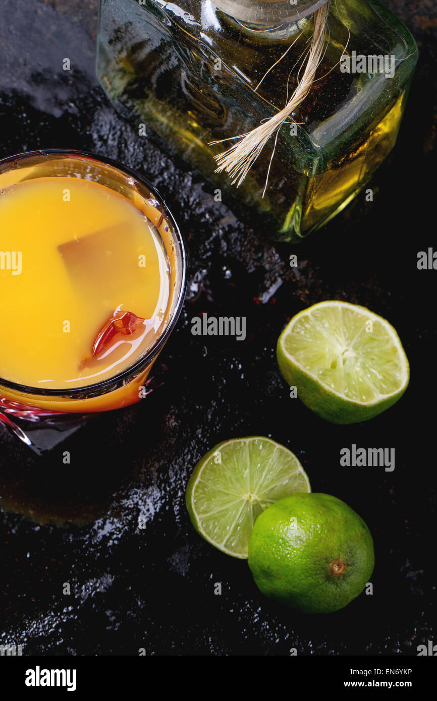 Glass of tequila sunrise cocktail, served with bottle of tequila anejo