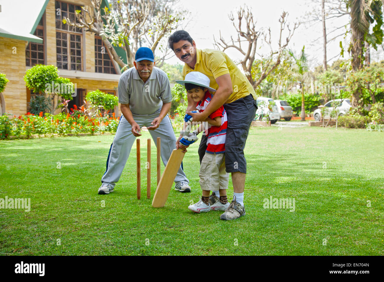 Young boy playing cricket with father and grandfather Stock Photo
