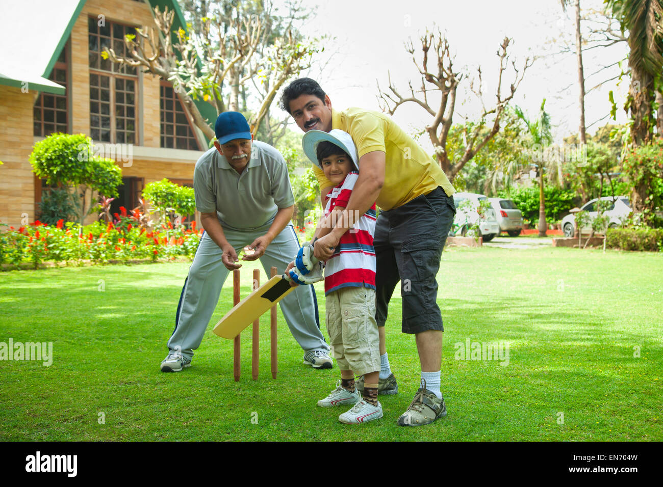 Young boy playing cricket with father and grandfather Stock Photo