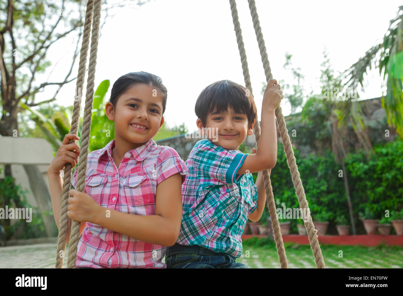 Portrait of brother and sister sitting on a swing Stock Photo - Alamy