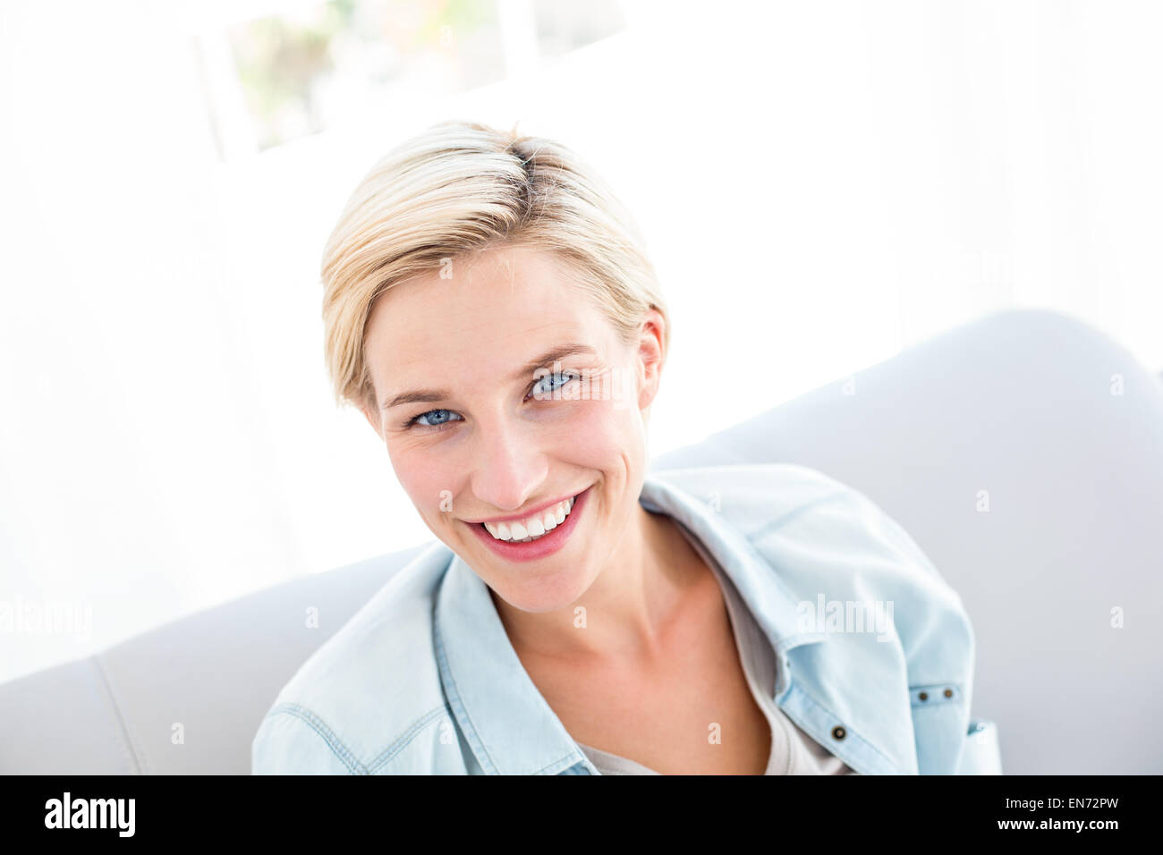Pretty blonde woman sitting on the couch and smiling at the camera ...