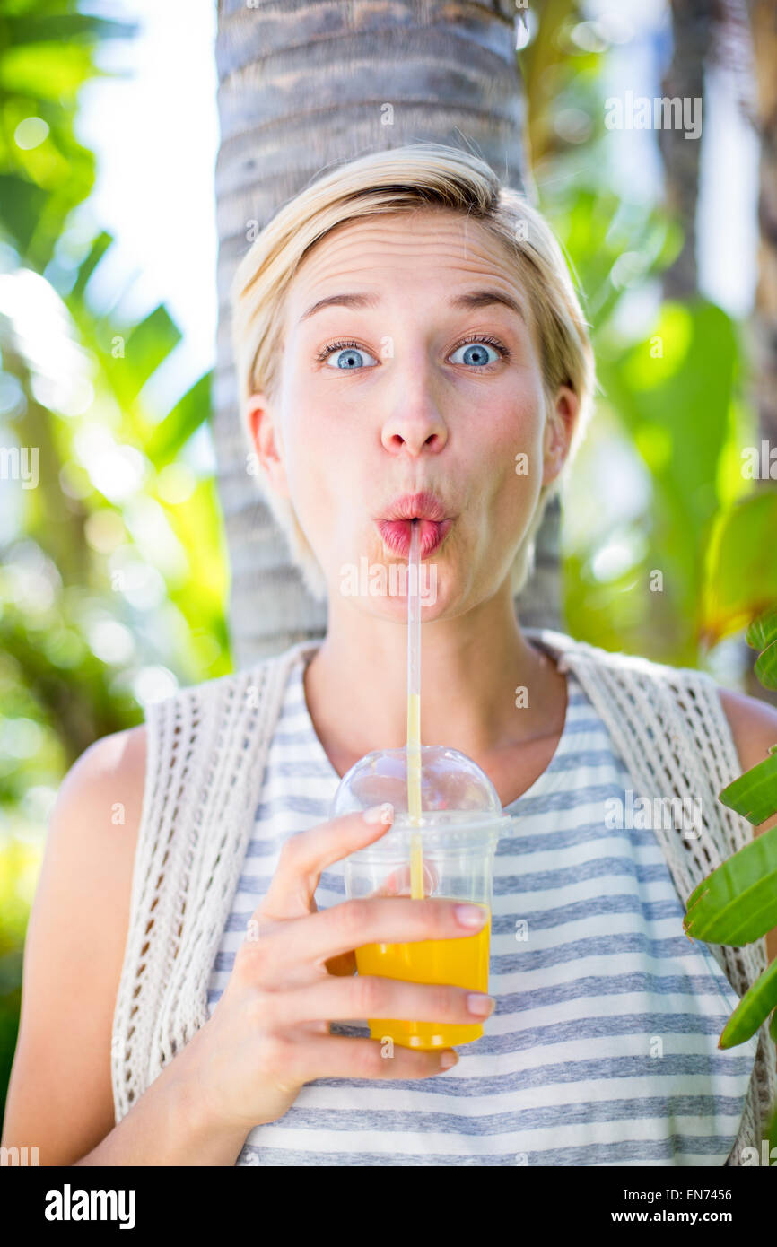Pretty blonde woman smiling at the camera and drinking orange juice Stock Photo