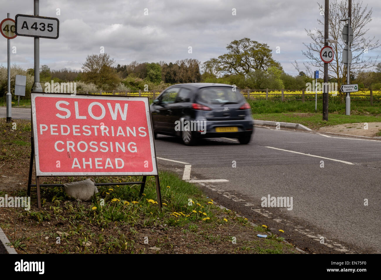 A 'Slow. Pedestrians Crossing Ahead' traffic sign on a main road outside Cirencester, as a car goes past motion blur road safety Stock Photo