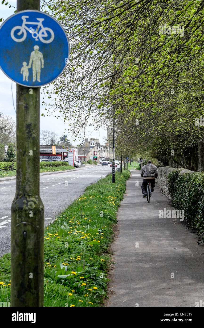 Rear view of a male cyclist on a shared pedestrian footpath and cyclepath with blue sign in the foreground on a main road. Stock Photo