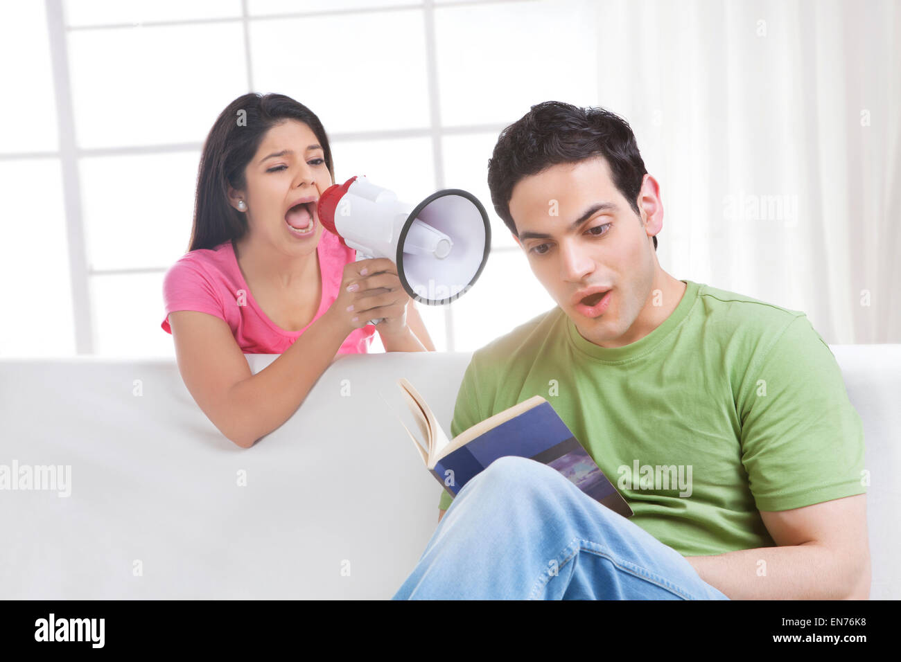 Young man reading while young woman is screaming into a megaphone Stock Photo