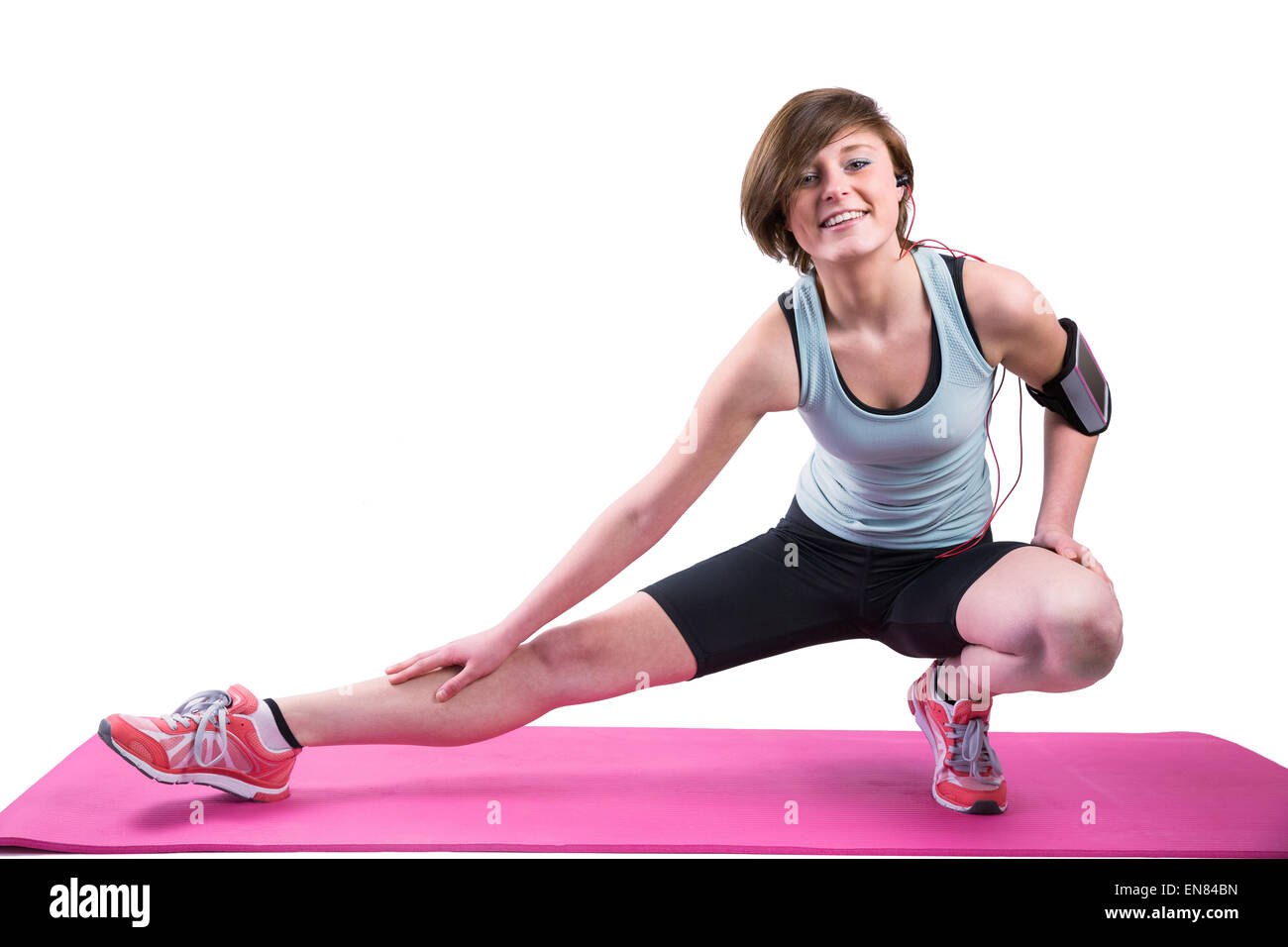 Pretty brunette looking at camera and stretching her leg on exercise mat Stock Photo