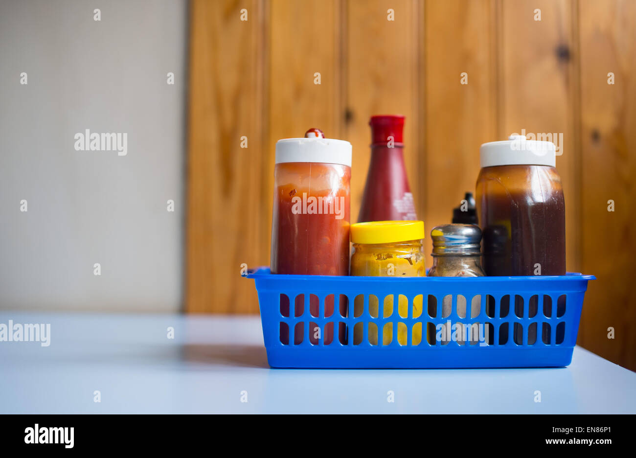 A cage in a cafe containing salt, pepper and various sauces including mustard, brown sauce, vinegar and ketchup. Stock Photo