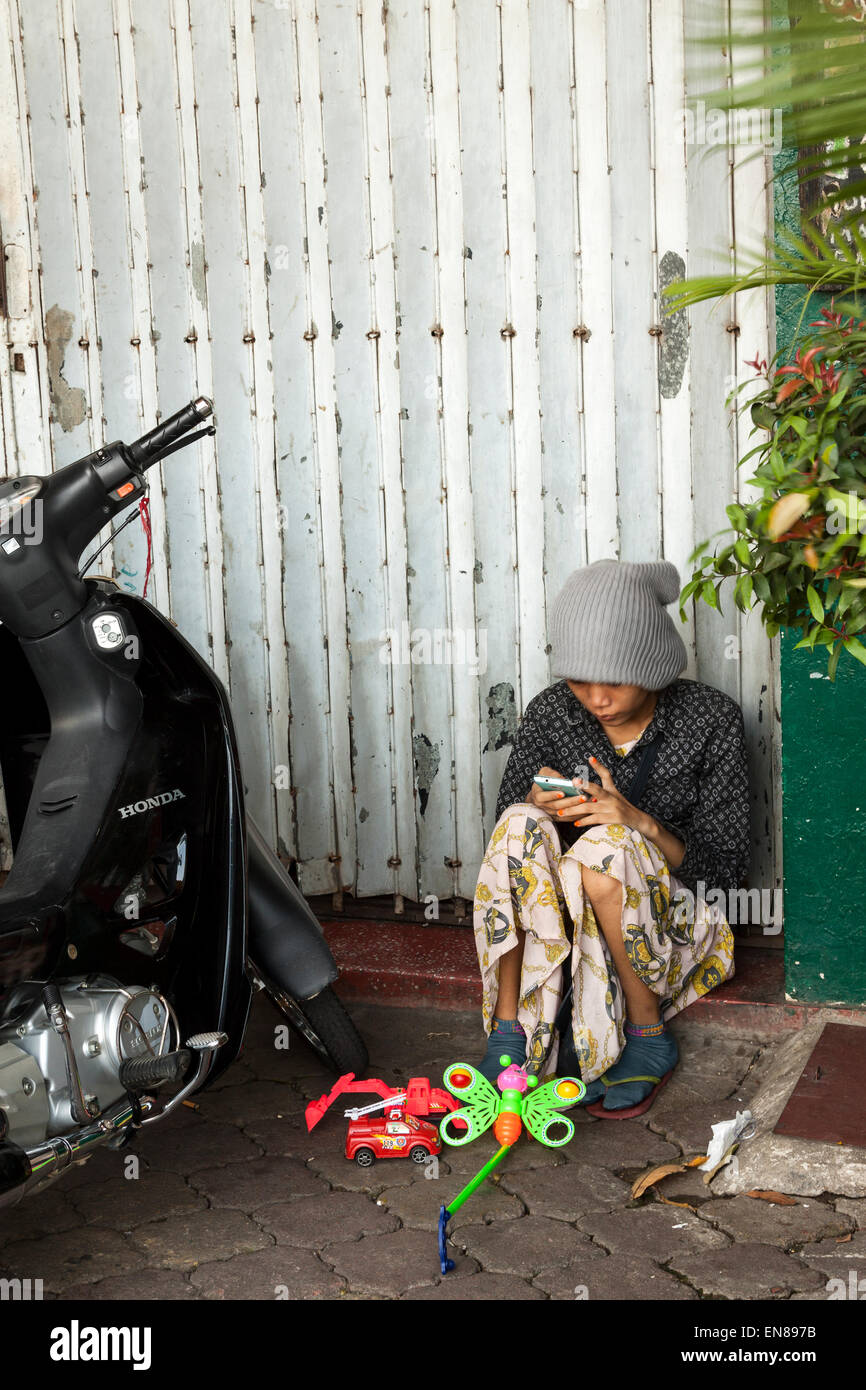 A Cambodian girl play on mobile phone while selling toys on the street - Phnom Penh, Cambodia, Asia. Stock Photo