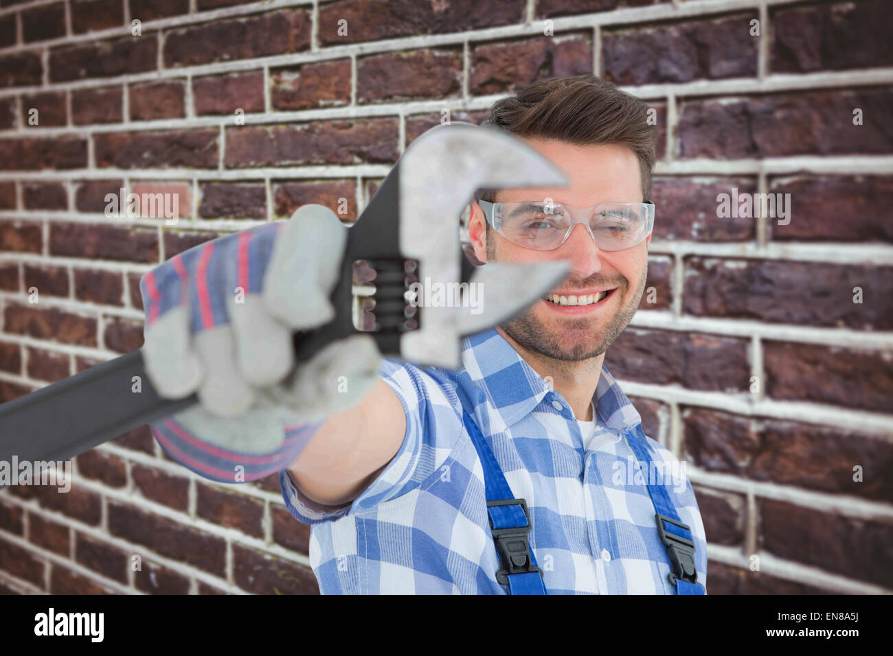 Composite image of handyman wearing protective glasses while holding wrench Stock Photo