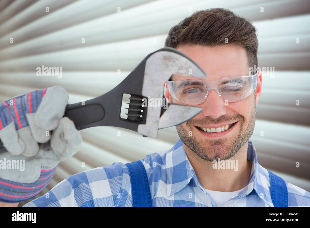 Composite image of confident repairman wearing protective glasses while holding wrench Stock Photo