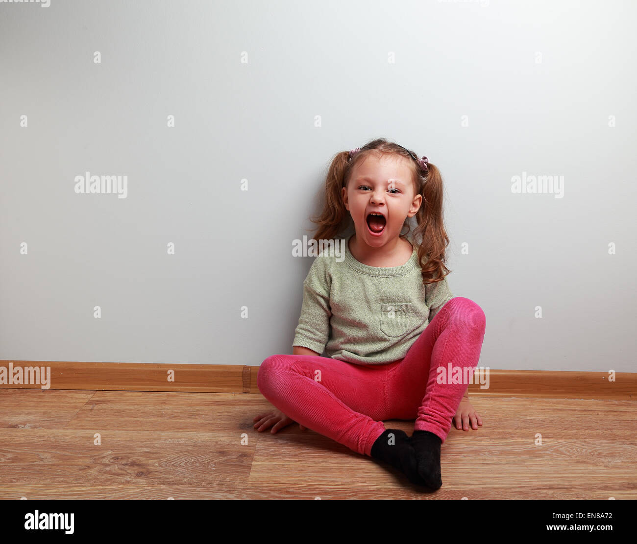 Happy crying kid with open mouth sitting on the floor in fashion clothes Stock Photo