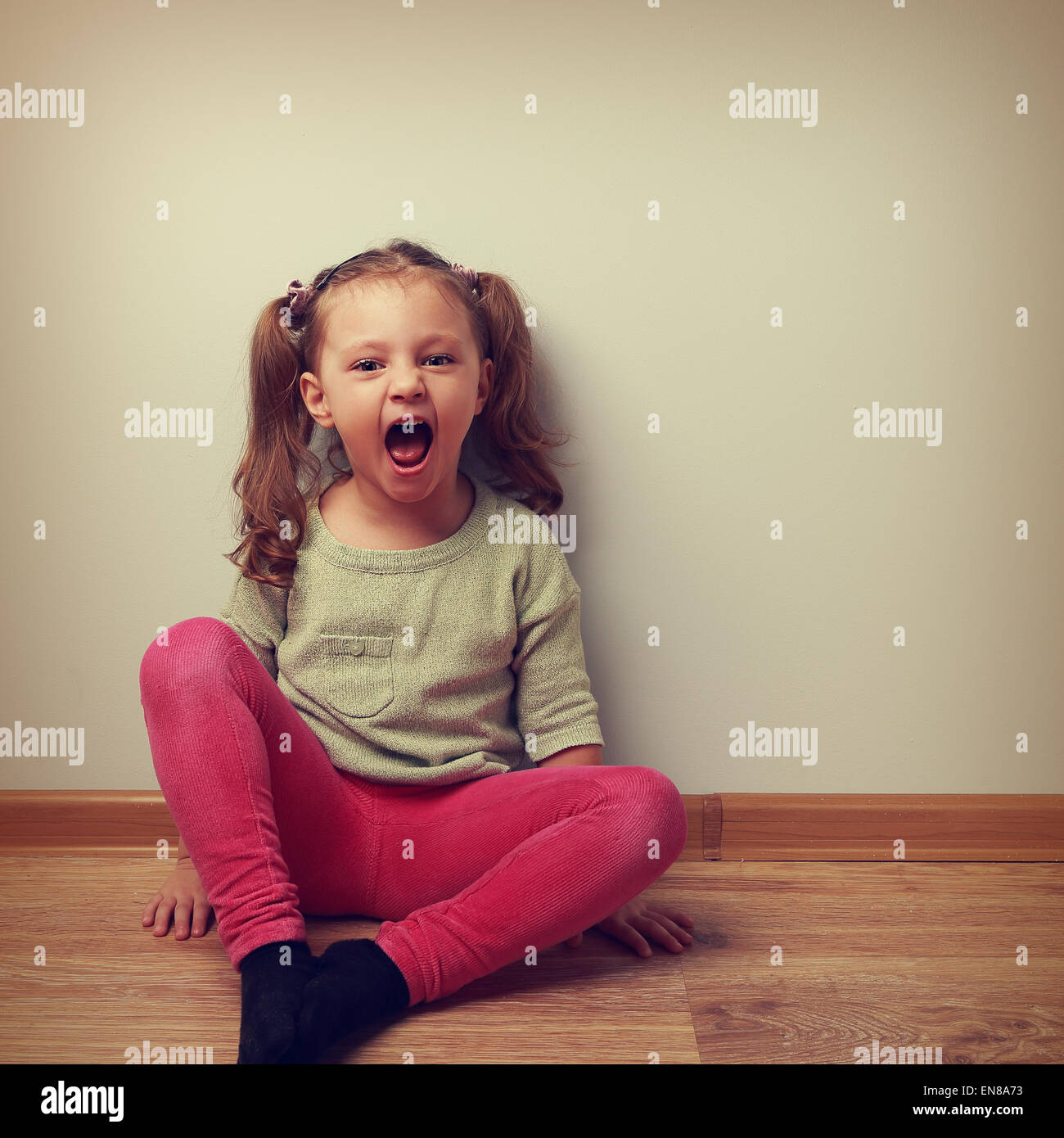 Happy crying kid with open mouth sitting on the floor in fashion clothes. Vintage color portrait Stock Photo