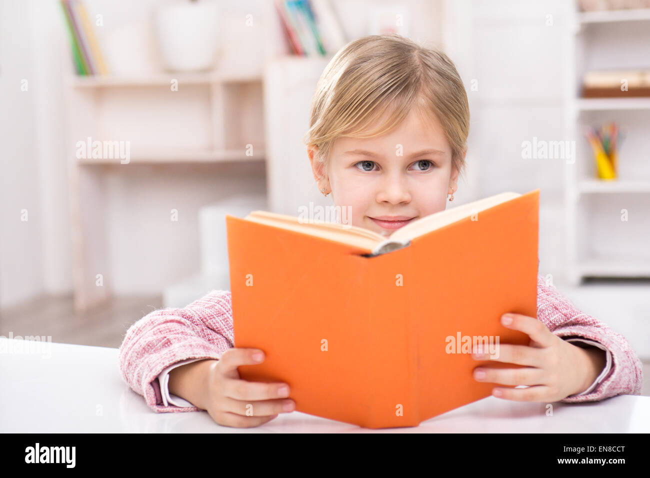 Smiling girl sitting at table and reading book Stock Photo - Alamy
