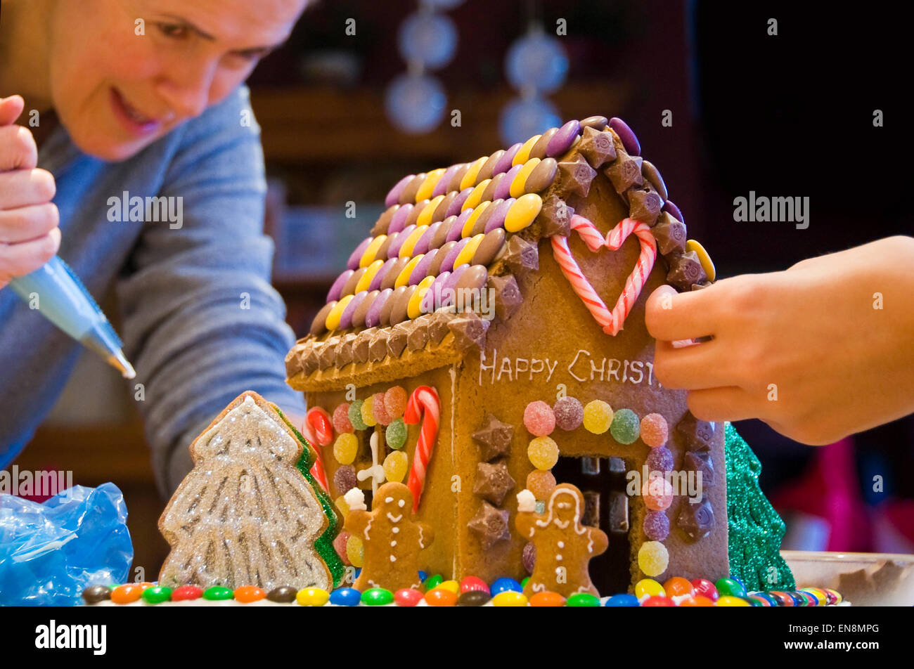 Horizontal view of a gingerbread house being decorated by a mother and daughter for Christmas. Stock Photo