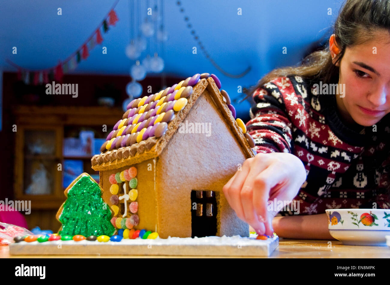 Horizontal view of a gingerbread house being decorated by a young girl for Christmas. Stock Photo