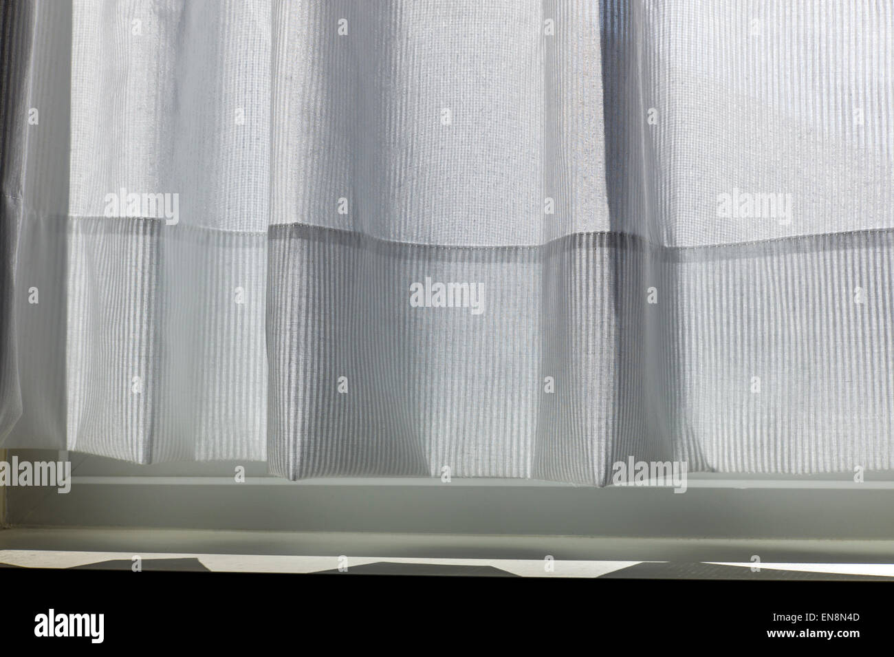 Sunlight creates abstract patterns on a delicate white cotton window curtain Stock Photo