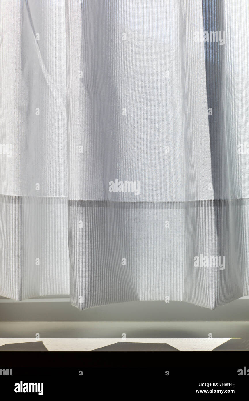 Sunlight creates abstract patterns on a delicate white cotton window curtain Stock Photo