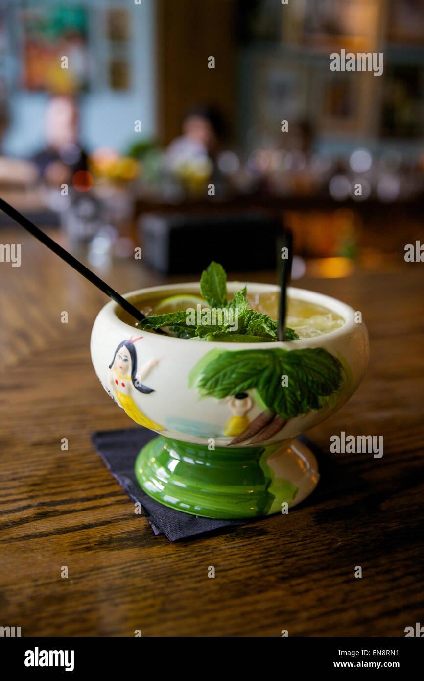 A tropical cocktail in a tiki cup with two straws sits on a bar. Stock Photo