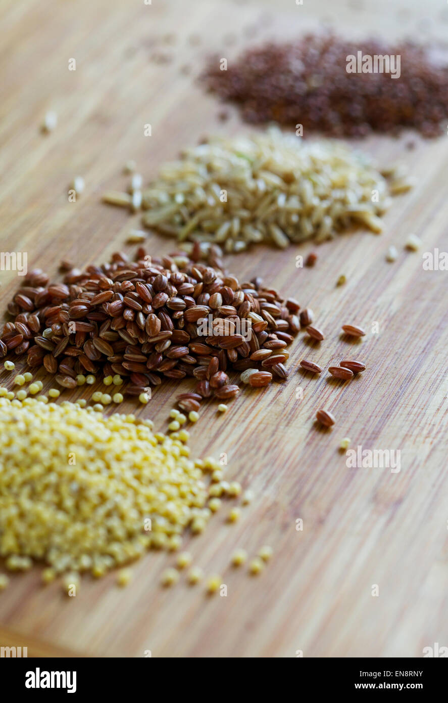 Four piles of uncooked whole grains including millet, red rice, brown rice and red quinoa. Stock Photo