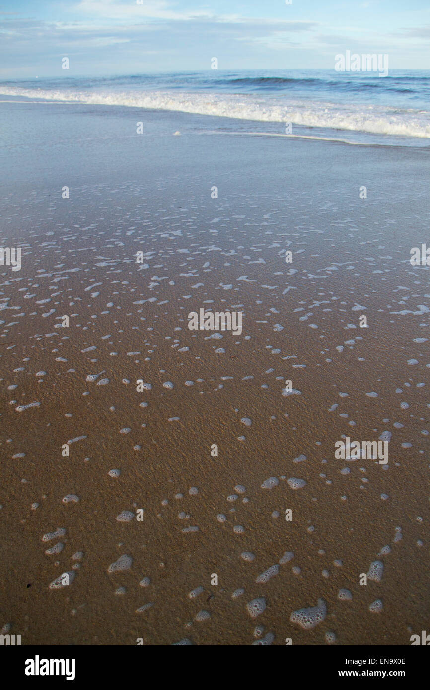 A foamy, outgoing ocean tide pulling back from a dark, sandy beach Stock Photo
