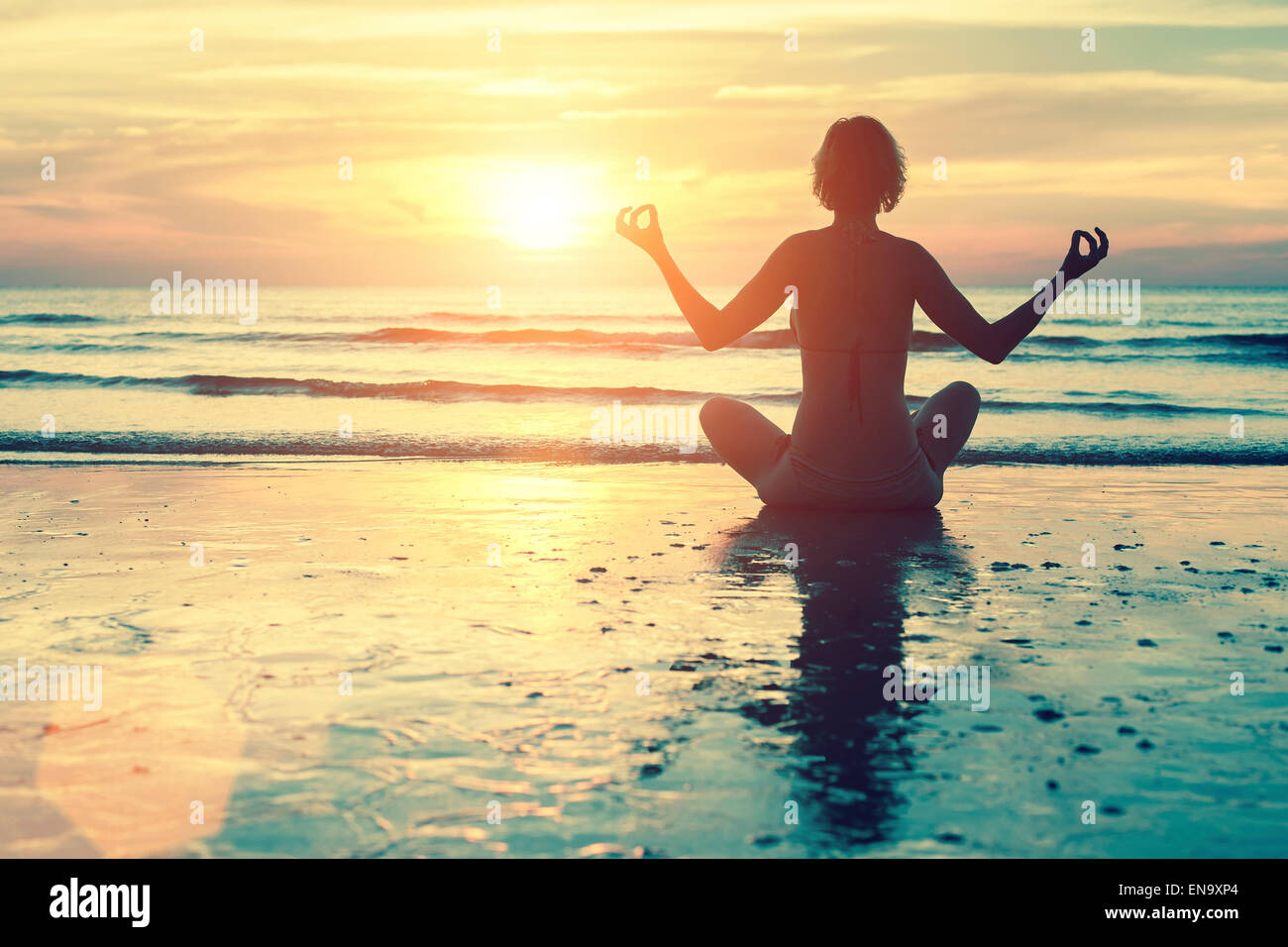 Female silhouette in yoga meditation pose at amazing sunset on the sea ...