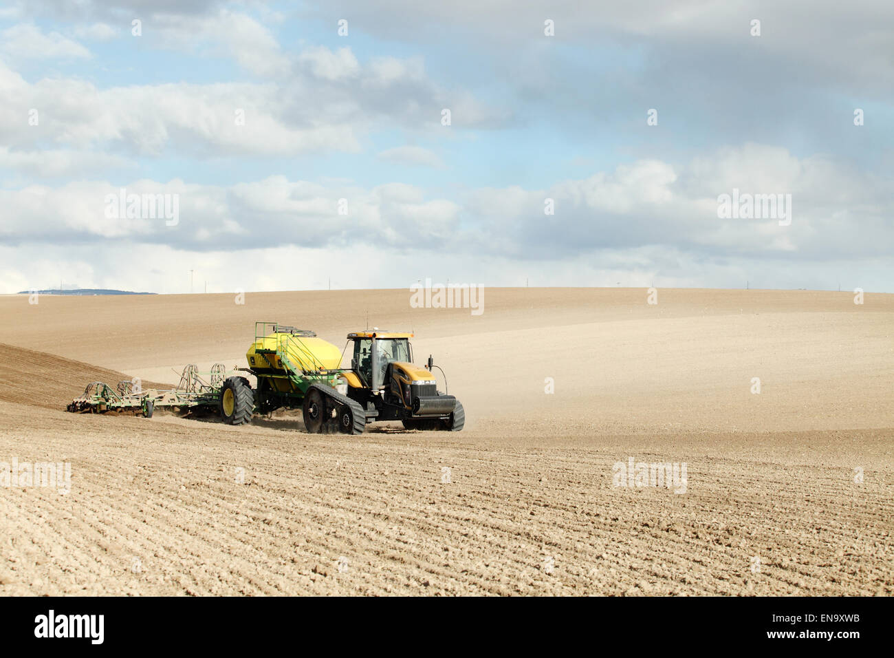 Farm machinery planting rows of wheat on a windy spring day in the fertile farm fields of Idaho. Stock Photo